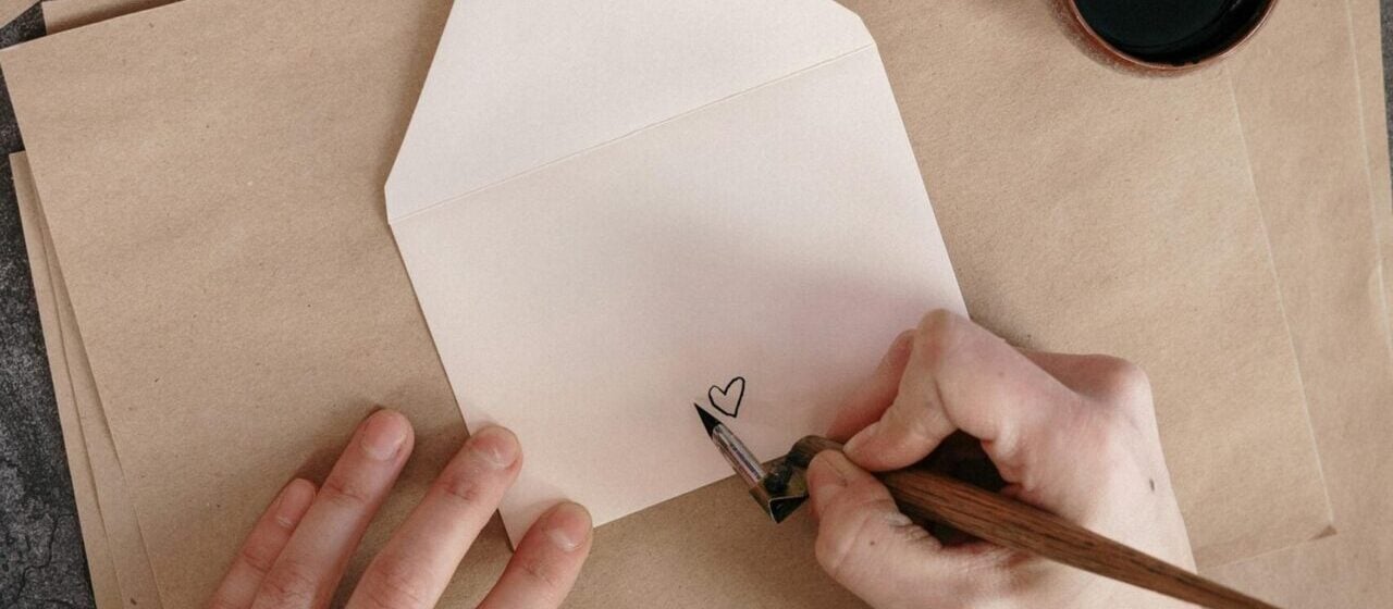 persona dibuja un corazón con tinta negra en el reverso de un sobre de papel para enviar cartas