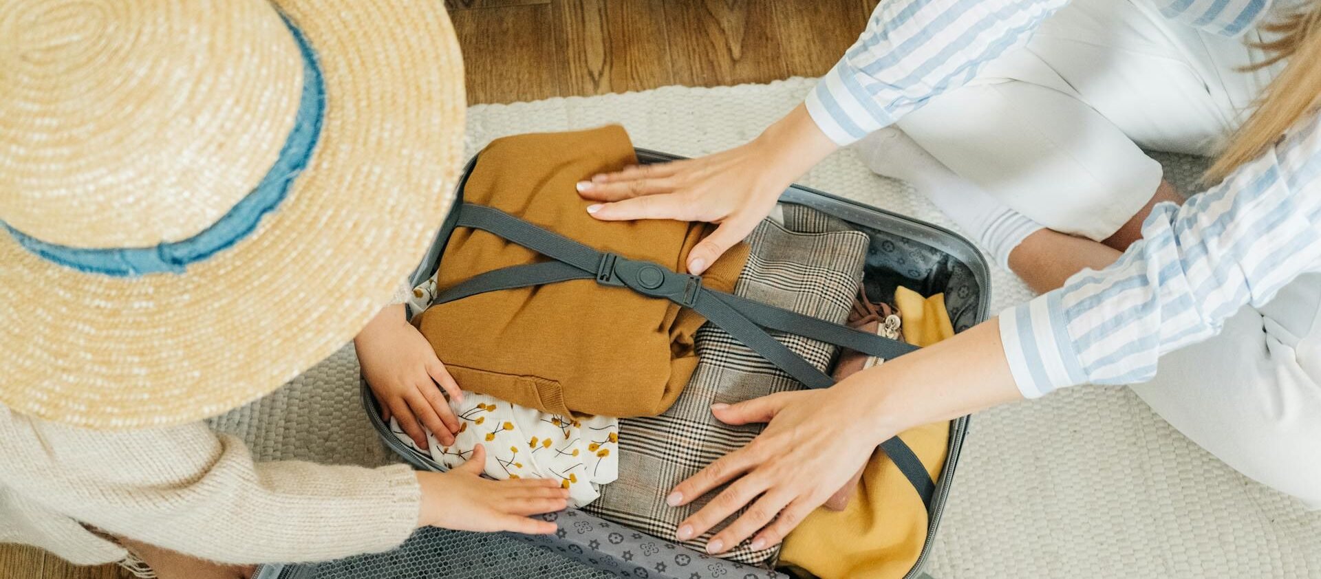 una maleta abierta en el suelo mientras madre e hija guardan ropa para viajar