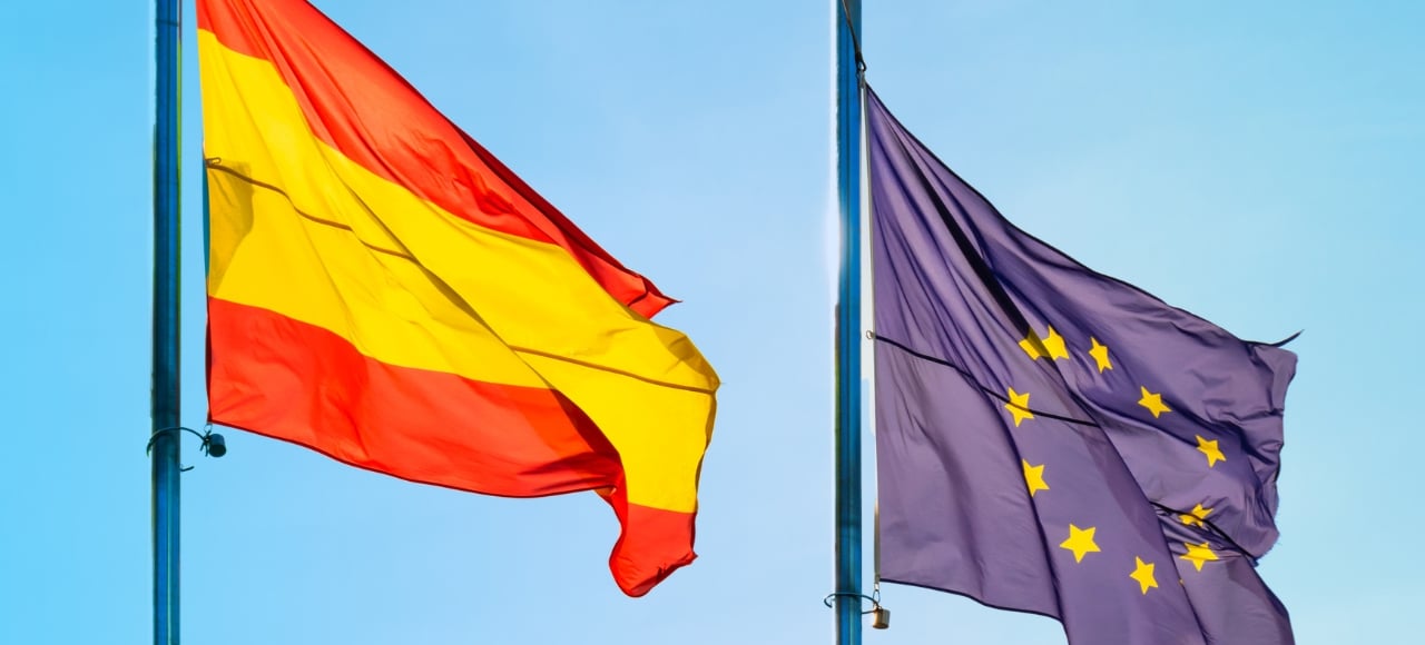 Bandera de España y bandera de la Unión Europea tras un cielo azul. Nacionalidad española