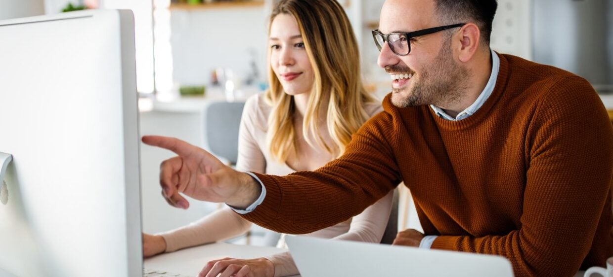 Dos socios miran en una computadora sus planes para emprender en España mientras sonrien