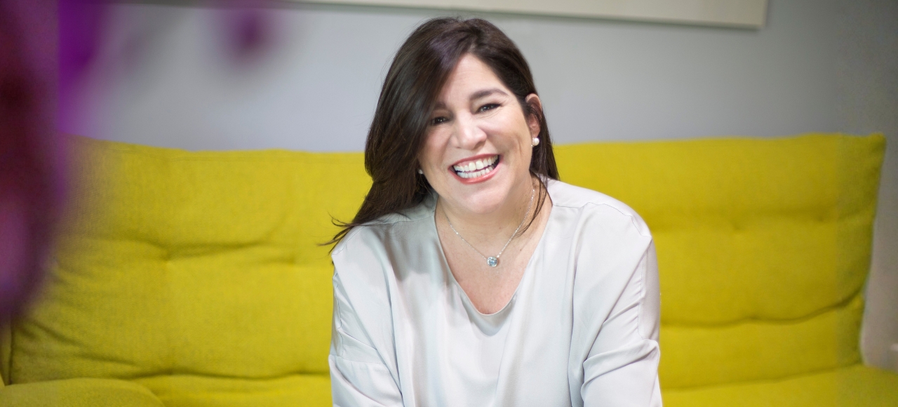 Carolina Godayol sonríe ampliamente, sentada en un sofá amarill